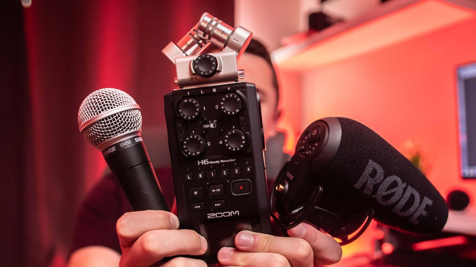 guy holding up a vocal microphone, an effects pedal, and an instrument mic showcasing gear you can get with sound equipment rental